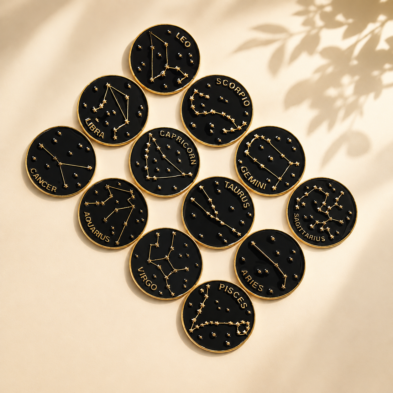 Black and gold zodiac constellation pins arranged on a warm cream background with soft natural light and botanical shadows.